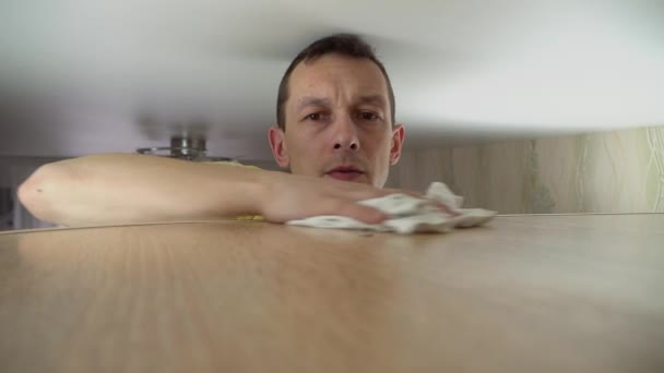 käsite siivous talon. mies pyyhkii pölyä korkeasta kaapista kotonaan - Materiaali, video