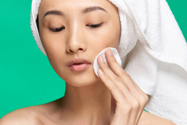 woman wipes her face with a cotton pad naked shoulders clean skin Green background - Фото, изображение