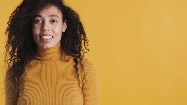 Attraente donna afro con i capelli ricci scuri in piedi vicino spazio copia per la vostra pubblicità e sorridente su sfondo giallo. Spazio per testo - Filmati, video