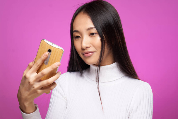 χαριτωμένο ασιατικό τηλέφωνο εμφάνιση στο χέρι τεχνολογία επικοινωνίας στο διαδίκτυο ροζ φόντο - Φωτογραφία, εικόνα