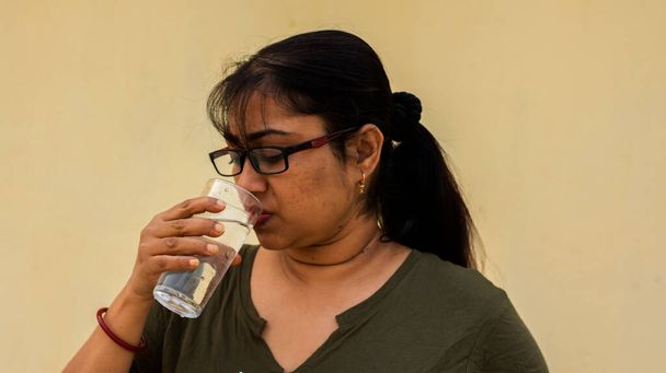 Una hermosa joven modelo india que tiene un vaso de agua. Concepto de agua potable, enfoque selectivo. Copiar espacio de texto. - Foto, imagen