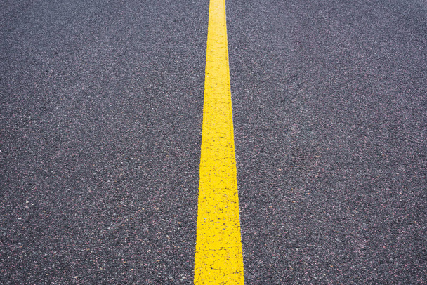 Pasek dzielący jest żółty. Gładka powierzchnia asfaltu z żółtym paskiem. Znaki i symbole drogowe. - Zdjęcie, obraz