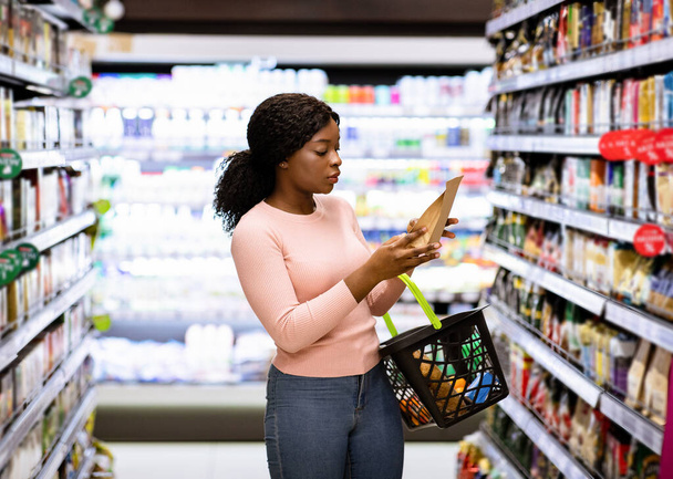 Mooie Afro-Amerikaanse vrouw maakt keuze uit producten in supermarkt - Foto, afbeelding