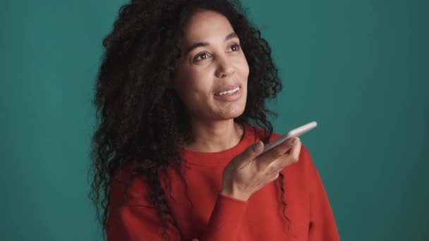 Attraente donna afroamericana che registra messaggi vocali ad un amico usando lo smartphone su sfondo blu. Comunicazione a distanza - Filmati, video