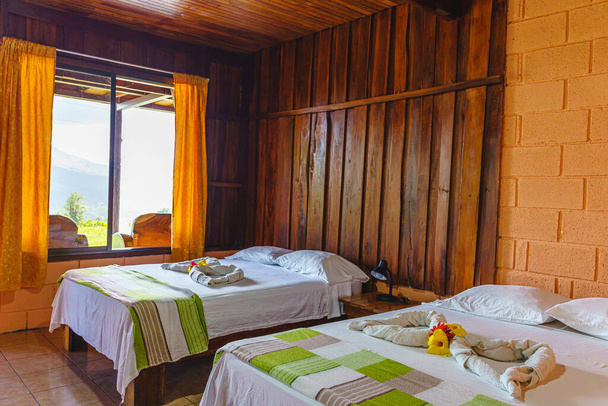 Habitación de hotel de montaña con una ventana con cortinas y toallas plegadas en las camas - Foto, Imagen
