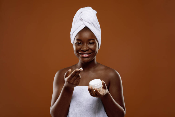 Hautpflege. Attraktive Afroamerikanerin mit offenem Glas und Feuchtigkeitscreme - Foto, Bild