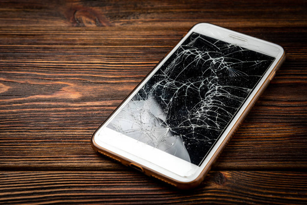 Rozbity szklany ekran smartfon na ciemnym drewnianym tle. - Zdjęcie, obraz