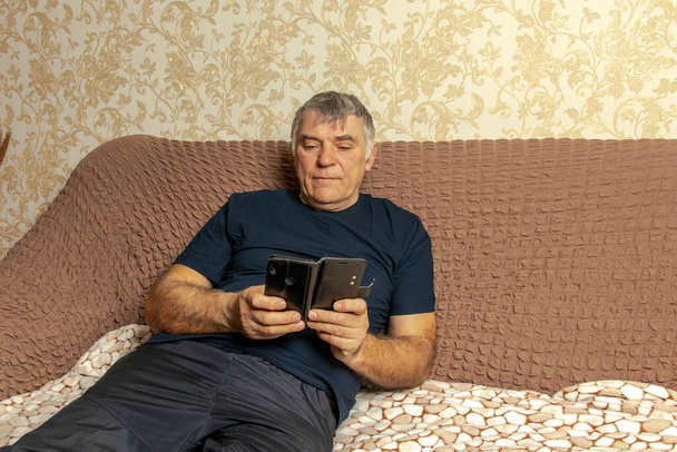 Šťastný starší muž se podívá na obrazovku mobilního telefonu, prohlíží si bezdrátový internet. Starší lidé doma používají internetové technologie - Fotografie, Obrázek