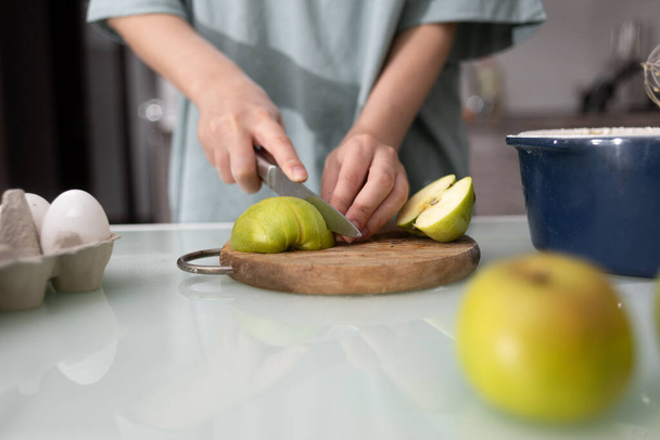 Close-up van de hand van een vrouwelijke chef die appels snijdt voor een taart in de thuiskeuken. Zelfgemaakt bakproces en ingrediënten voor koekjes, taarten, fruitmanden. Koken thuis. - Foto, afbeelding