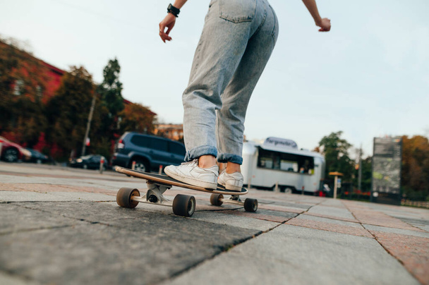 Rückenansicht, abgeschnittene Aufnahme einer Skateboarderin, die ein langes Brett auf einem Betonpflaster reitet. Stadtstraße im Hintergrund. - Foto, Bild