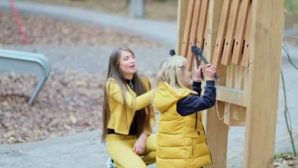 mom or nanny plays with her daughter on the playground. happy childhood concept. little girl playing street musical instruments - Footage, Video