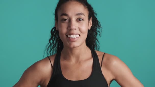 Fiatal vonzó afro-amerikai nő öltözött sport melltartó keres boldog mosolygós kamera edzés után a kék háttér. Sportkoncepció - Felvétel, videó