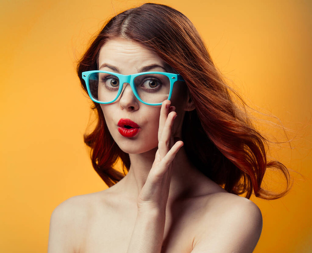 šťastná žena v modrých brýlích s jasným make-up na oranžovém pozadí - Fotografie, Obrázek