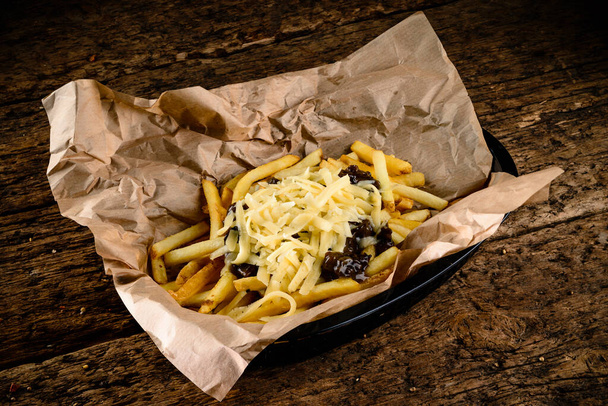 Golden yummy deep French fries on kraft baking sheet paper and serving tray to eat, lifestyle. french fries on kraft paper rustic style on old wooden background - Photo, image