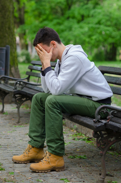 Неспокійний молодий чоловік сидить у парку
 - Фото, зображення