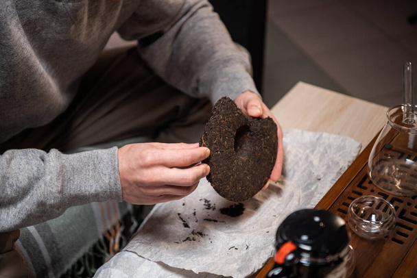 De cerca. Un vendedor de té rompe un pedazo de té negro fuerte con una aguja de té para la venta en una tienda de té. - Foto, imagen