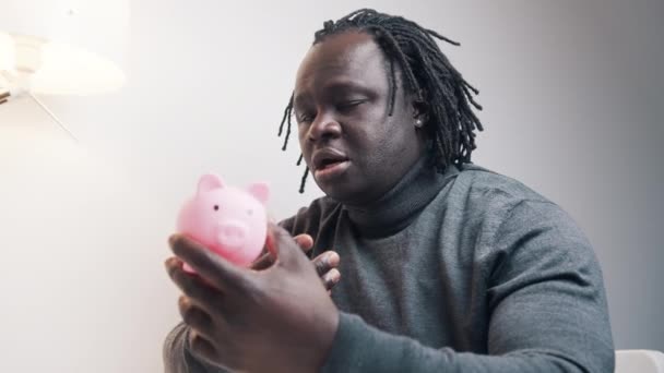 Faillissementsconcept. Trieste Afrikaanse Amerikaanse zwarte man kijkt naar lege spaarvarken bank en schudt zijn hoofd - Video