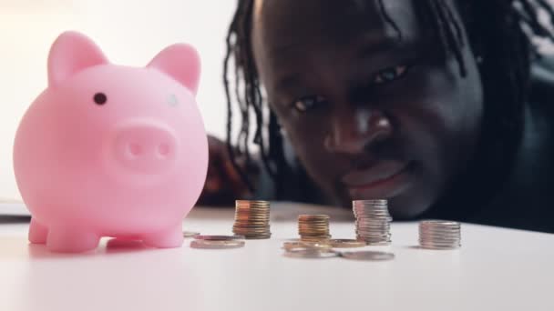 Financiële beslissingen. Een man die zijn spaargeld telt. Close-up van de varkensbank omringd door munten.  - Video