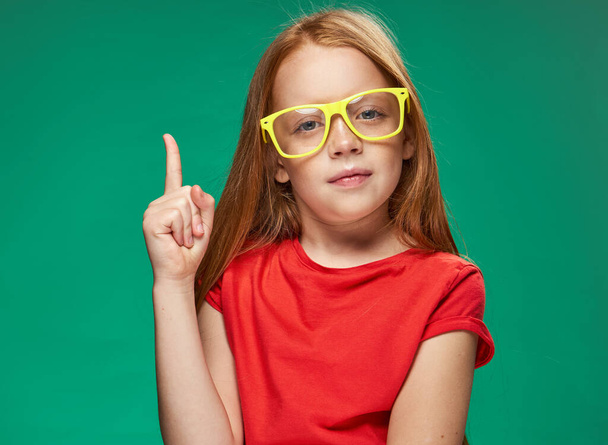 menina com cabelo vermelho vestindo óculos amarelos posando emoções recortadas vista estúdio escola - Foto, Imagem