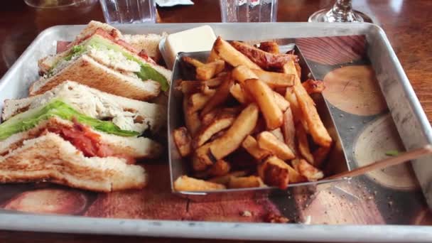 Clubsandwich met kippenvlees, frietjes op een bord met mosterd en ketchup. Clubsandwich op een wit bord met gesneden toast brood, mayonaise tomaten, sla, kaas en spek. - Video