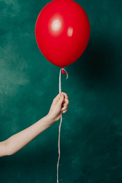 φουσκωτό κόκκινο μπαλόνι σε γυναικείο χέρι σε πράσινο φόντο close-up - Φωτογραφία, εικόνα