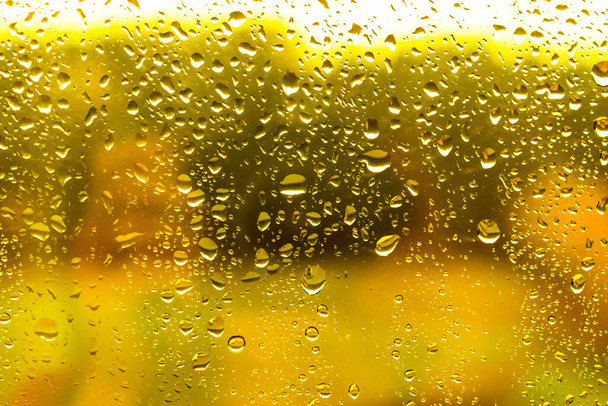 Yağmurlu günlerde sarı arka planlı bardağa bir damla su damlatın. - Fotoğraf, Görsel