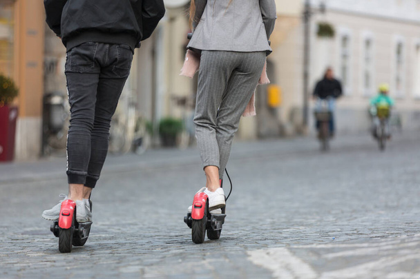 Visão traseira de adolescentes fashinable moda irreconhecível montando scooters elétricos de aluguel público no ambiente urbano da cidade. Novos transportes públicos modernos e ecológicos em Liubliana, Eslovénia. - Foto, Imagem
