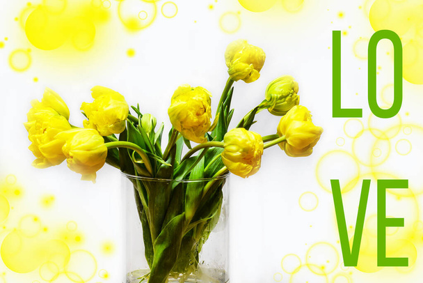 Bouquet di splendidi tulipani gialli in un vaso di vetro, isolato su bianco.Campione di fiori primaverili per il tuo progetto. Biglietto d'auguri primavera. Manifesto dell'evento con l'iscrizione LOVE. - Foto, immagini