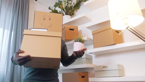 Волнующий черный мужчина с картонной коробкой над головой переезжает в новый дом - Кадры, видео
