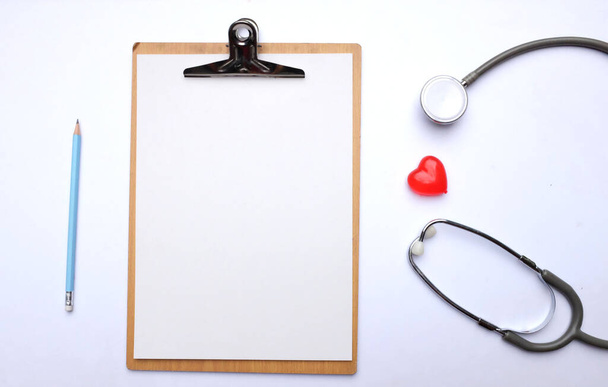 Stethoskop mit rotem Herz, Klemmbrett, Bleistift auf dem weißen Arzttisch. - Foto, Bild