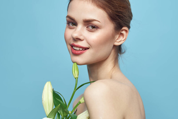 Vrouw met witte bloem op blauwe achtergrond bijgesneden weergave van naakte schouders - Foto, afbeelding