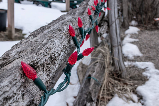 Un enchevêtrement d'ampoules rouges de Noël ne s'allume pas sur une vieille clôture en bois rachitique à London, au Canada. Décorations rustiques sur le thème des vacances pour la saison. - Photo, image