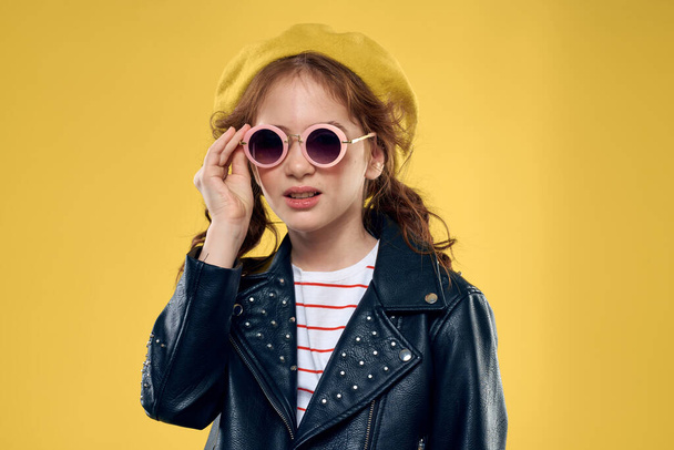 Cheerful little girl in sunglasses and hat lifestyle studio yellow background fashion - 写真・画像
