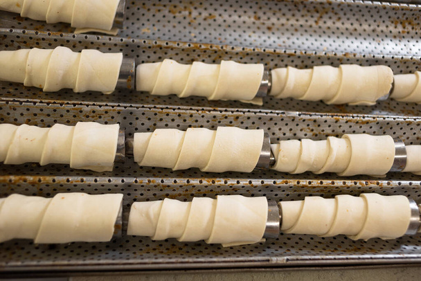 Rolls of raw puff pastry on a metal cone. Baking in a pastry shop. Bakery and flour products. - Photo, Image
