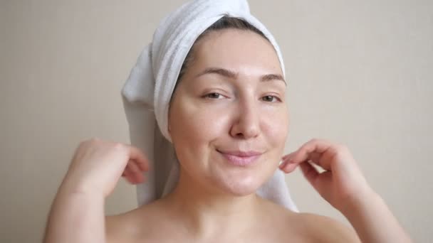 Νεαρή γυναίκα με λευκή πετσέτα στο κεφάλι να χαϊδεύει το πρόσωπο - Πλάνα, βίντεο