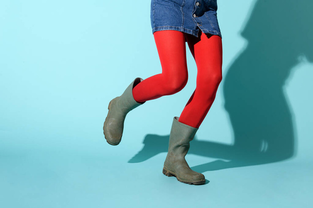 Ноги женщины, бегущей в ярко-красных леггинсах и зеленых резиновых сапогах на синем фоне студии с тенью и копирайтом - Фото, изображение