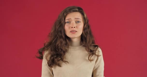 Female studio portrait, angry caucasian woman frustrated girl screams from stress tension problems feels horror hopelessness fear surprise shock expresses gestures rage standing near red background - Footage, Video