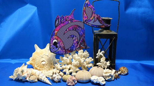 um peixe pequeno nada em um fundo marinho azul entre conchas, corais, esqueletos de ouriço e lâmpadas velhas - Foto, Imagem