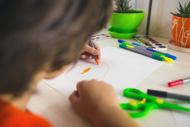 Der Junge zeichnet mit Filzstiften auf Papier, das Kind beschäftigt sich mit Kreativität, das Kind erledigt seine Hausaufgaben, linkshändiger Tag - Foto, Bild