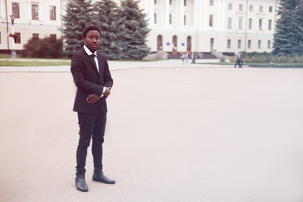 Portrait horizontal de jeune homme d'affaires afro-américain debout dans la rue les mains croisées et regardant la caméra. Image avec espace de copie et les gens passent sur l'arrière-plan. - Photo, image
