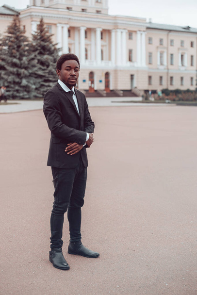Portrait vertical de jeune homme d'affaires afro-américain sérieux se tient dans la rue avec les mains croisées et regarde dans la caméra. Concept d'entreprise. Millennial guy en costume et cravate. - Photo, image