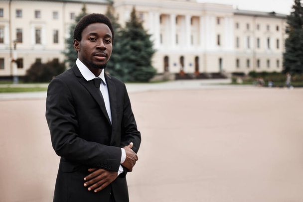 Foco seletivo do jovem empresário afro-americano confiante olhando para a câmera. Homem negro com as mãos dobradas em pé na rua. Imagem com espaço de cópia.  - Foto, Imagem