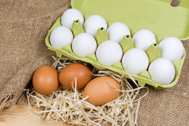 Ruskeat kananmunat puulastujen päällä ja valkoiset munat pahvikotelossa, joka on valmistettu kierrätyspaperimassasta säkkikankaan lähikuvassa  - Valokuva, kuva