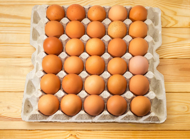 Brown chicken eggs in cardboard egg tray packaging made of recycled paper pulp on wooden rustic table, top view - Photo, Image