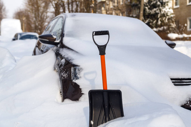 pala de nieve de plástico frente al coche cubierto de nieve en la soleada mañana de invierno - Foto, imagen