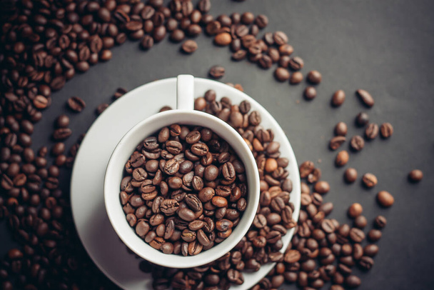Kaffeebohnen in einer Tasse und weißen Untertassen grauen Hintergrund Nahaufnahme - Foto, Bild