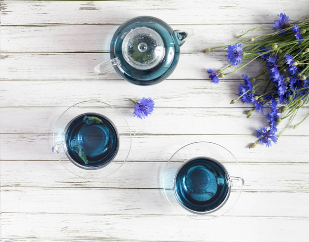 Cam bardaklar ve çaydanlık Kelebek bezelye çayı. Beyaz ahşap arka planda Anchan. Bir buket mavi çiçekle - Fotoğraf, Görsel