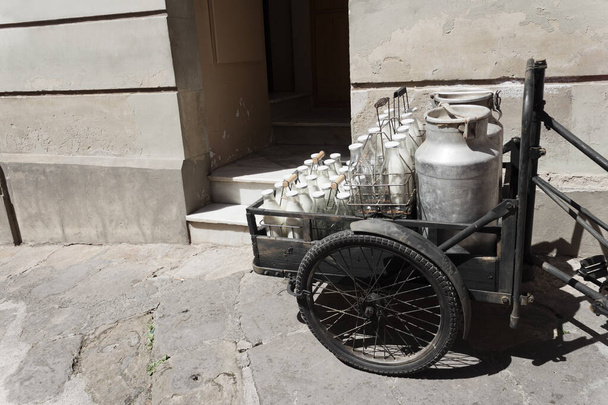 Bottles and aluminum cans of milk for delivery in vintage rusty milkman bicycle. - Photo, Image