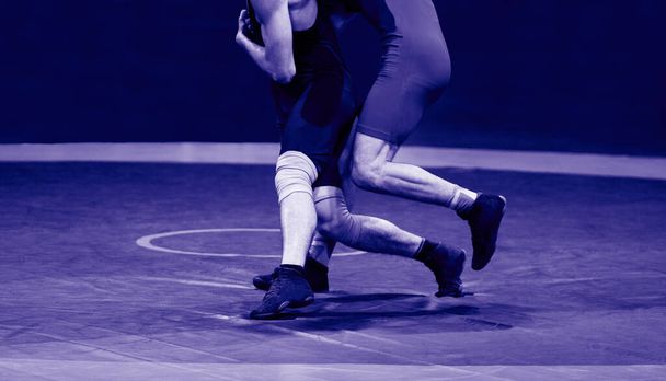 Dvě silné zápasnické nohy na modrém wrestlingovém koberci v tělocvičně. Filtr modré barvy - Fotografie, Obrázek