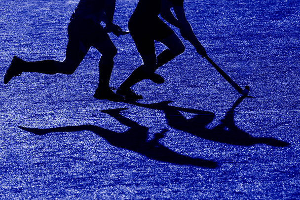 Silhueta. A sombra de um jogador de hóquei está correndo com uma vara de hóquei em um campo de hóquei. Filtro de cor azul - Foto, Imagem